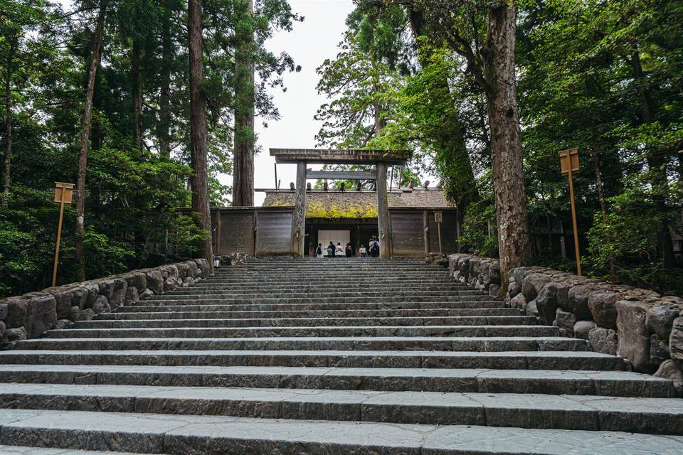 伊勢神宮 内宮。杉木立に囲まれた石段の上に、鳥居と茅葺き屋根の門が見える