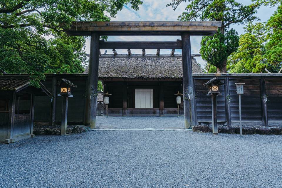 伊勢神宮 外宮。玉砂利の先に立つ木の鳥居と、茅葺き屋根の神社の門